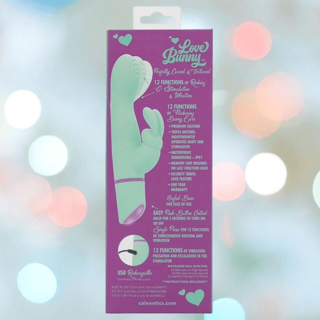 A package for the CalExotics Love Bunny Rockin’ “G” Bunny shows a light green rabbit-shaped device and product details in white text on a purple background with blurred pastel lights behind.