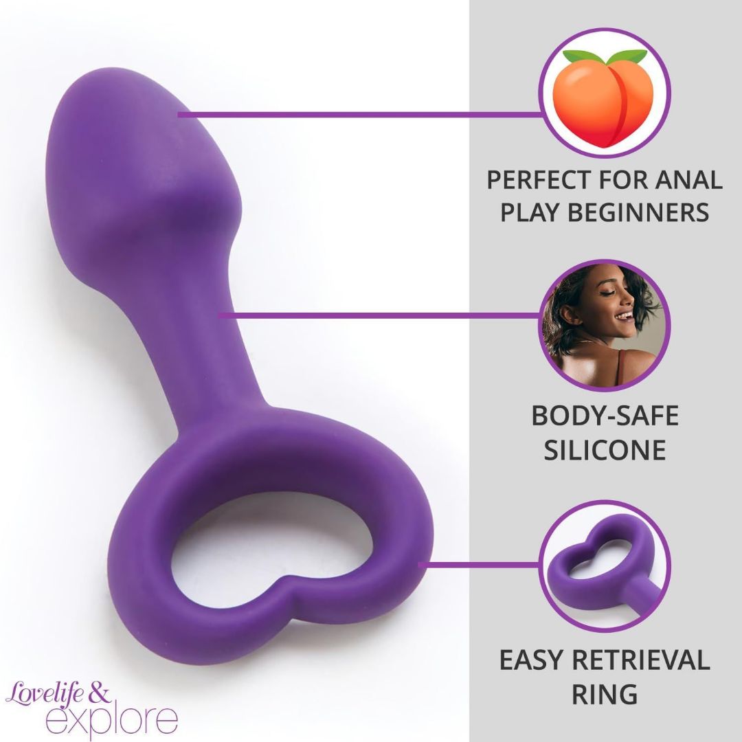 The OhMiBod LoveLife Explore Pleasure Anal Plug, showcased in a purple hue, features a heart-shaped retrieval ring. Emphasized by the text is its suitability for beginners in anal play, crafted from body-safe silicone material for added safety and comfort. The pleasure toy is designed with a stylized peach icon to enhance its aesthetic charm and ensure easy retrieval.