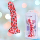 A Maia Juci Strawberry Themed Suction Dong 7" by Maia Toys, featuring a sturdy silicone design with a vibrant strawberry pattern and suction cup base, is pictured next to its packaging. The background is adorned with soft, multicolored bokeh lights.