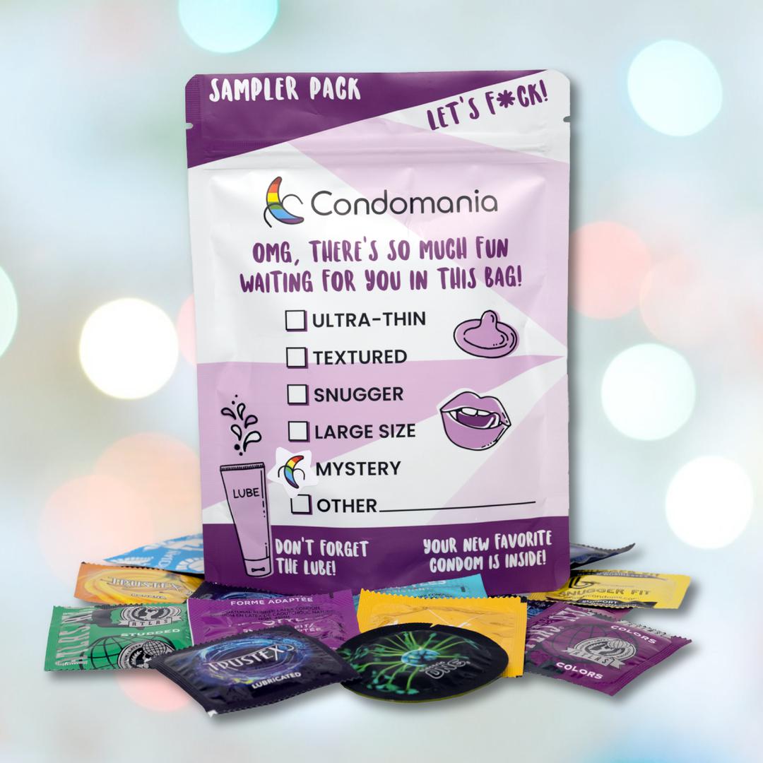 A sampler pack of Mystery Condom Sampler (12-Pack) from Condomania against a bokeh background. The package features colorful designs and text listing various condoms: ultra-thin, textured, snuggish, large size, and more. Assorted wrappers are scattered below—discover your new favorite condom here.