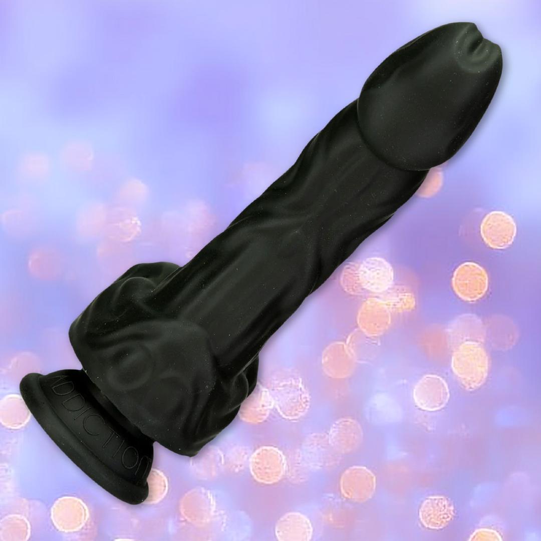 The BMS Naked Addiction Silicone Rotating & Thrusting Dildo - Noir 8.6", shown on a purple background with soft pink bokeh lights, features lifelike detail and a suction base for versatile solo or partnered play.
