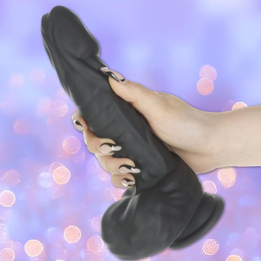 A hand with long, manicured nails holds the BMS Naked Addiction Silicone Rotating & Thrusting Dildo - Noir 8.6" against a soft, purple bokeh background. 1080