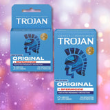 Two boxes of Trojan ENZ Armor Spermicidal Condoms by Trojan are shown against a sparkling pink background; one is a 3-count box of standard thickness condoms, and the other is a 12-count box. Both packages feature the blue Trojan helmet logo along with eye-catching promotional text.