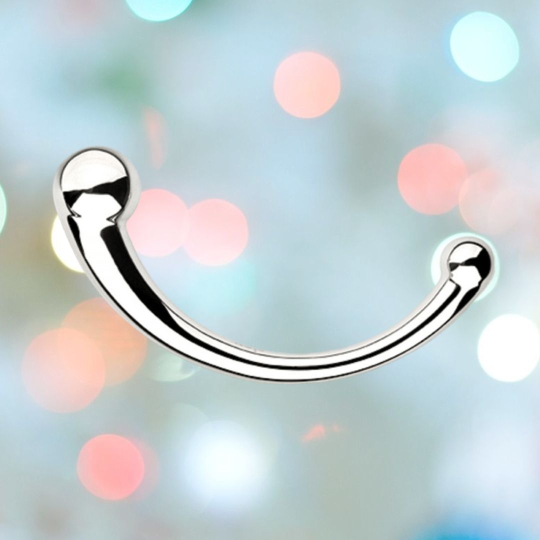 A curved, shiny metal object made of medical-grade stainless steel with ball-like ends is set against a background of blurry, colorful bokeh lights. The Njoy Pure Wand Non-Vibrating Metal G-Spot and P-Spot Massager has a smooth, reflective surface and is positioned perfectly in the center of the image.