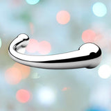 A sleek, polished silver object resembling a sophisticated hook or handle, crafted from medical-grade stainless steel, is centered against a blurred background featuring a mix of pastel and vibrant bokeh lights. The overall feel is modern and elegant, highlighting the impeccable design of the Njoy Pure Wand Non-Vibrating Metal G-Spot and P-Spot Massager from Njoy.