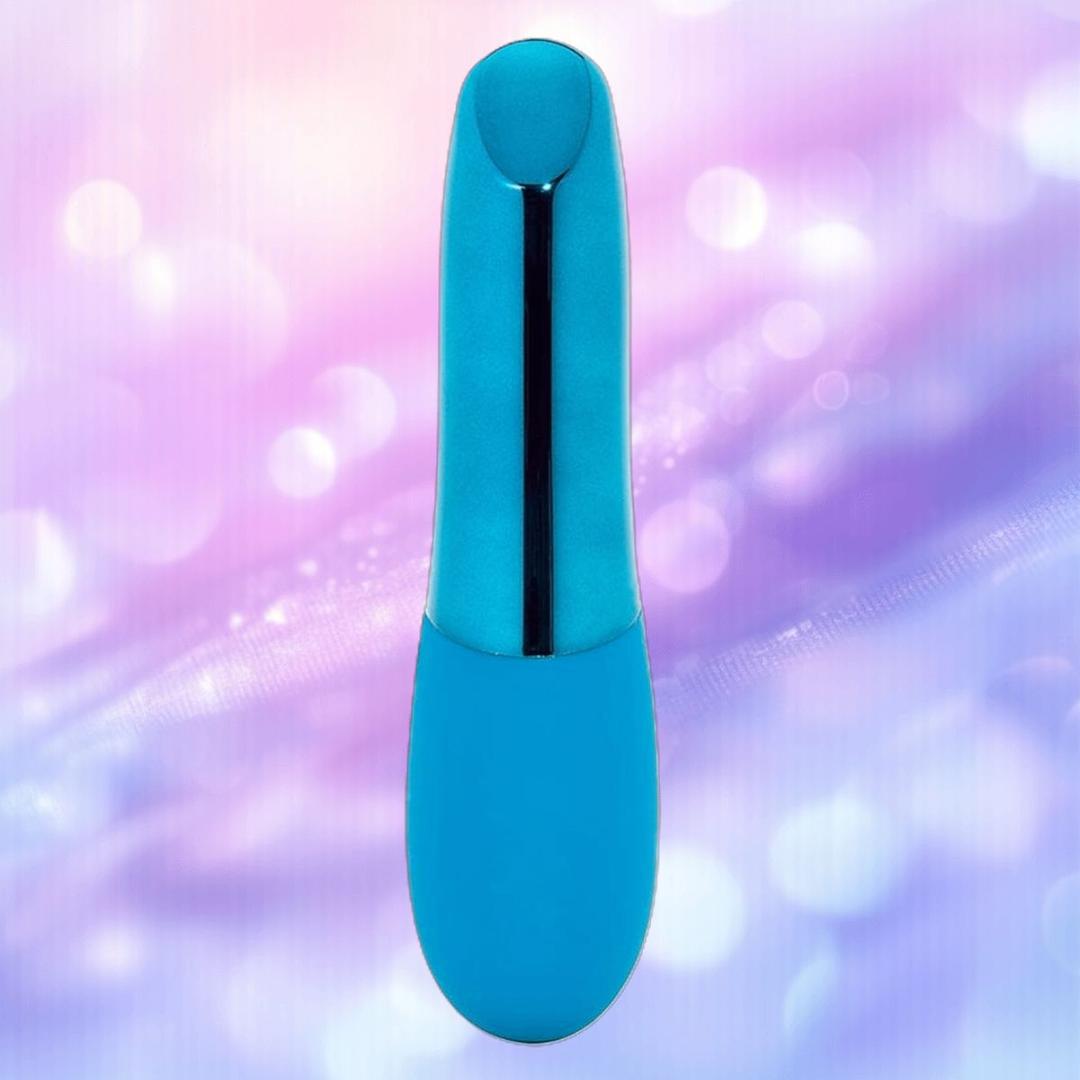 The Nu Sensuelle Nikita by NOVEL CREATIONS USA, a smooth deep turquoise cylindrical bullet vibe with a rounded top, is displayed against a softly blurred pastel purple and pink background.