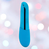 The Nu Sensuelle Nikita High-Power Nitro Bullet Vibrator by NOVEL CREATIONS USA features a deep turquoise, sleek cylindrical design with a shiny strip, shown against a blurred background with soft white and pink circular lights.