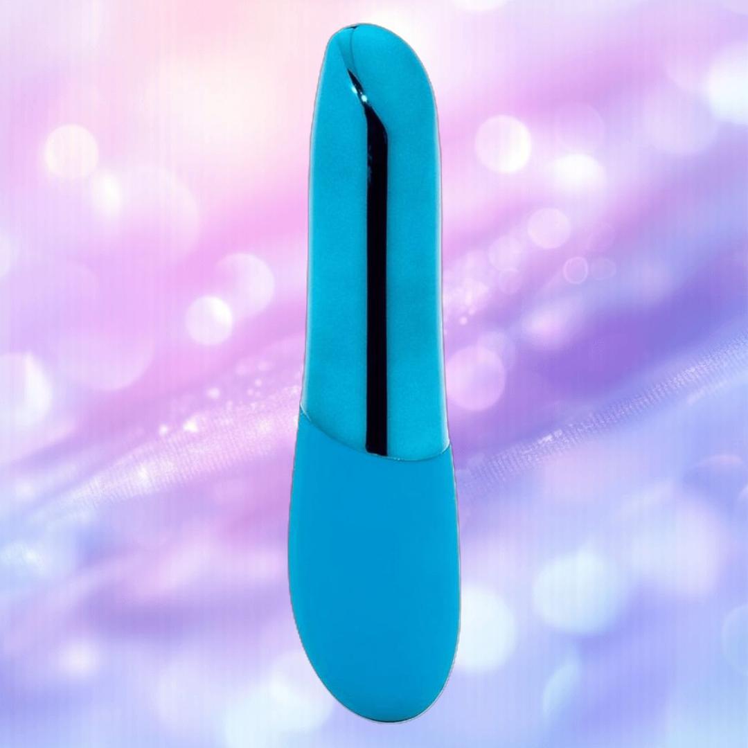 The Nu Sensuelle Nikita by NOVEL CREATIONS USA is a deep turquoise, curved bullet vibrator with a sleek, shiny stripe, displayed against a soft pastel purple and pink bokeh background.