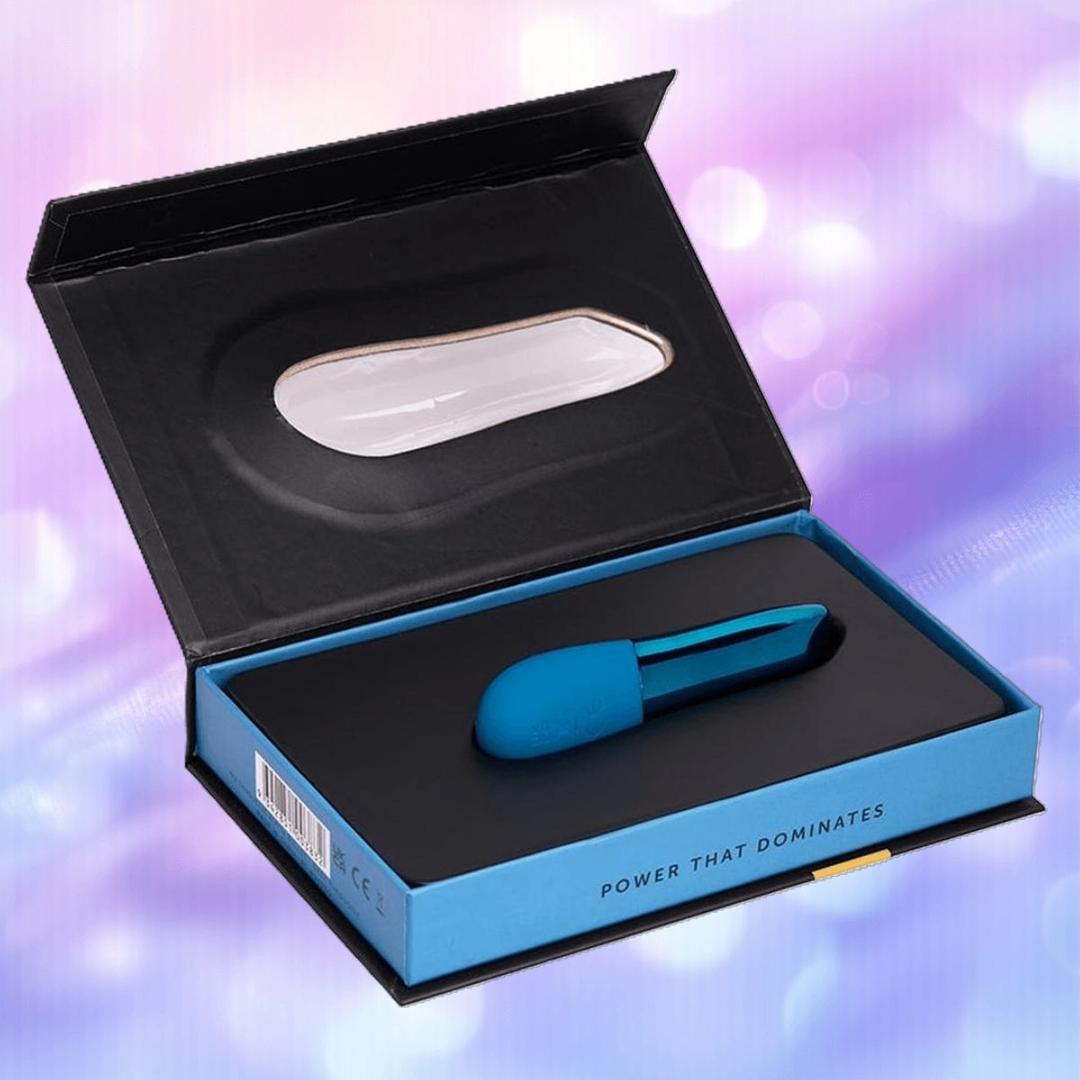 The Nu Sensuelle Nikita - Deep Turquoise by NOVEL CREATIONS USA is a waterproof vibrator in a sleek black and blue box with "Power That Dominates" on the edge, set against a softly blurred pastel background.