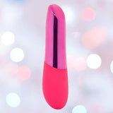 The Nu Sensuelle Nubii Raine Tapping Vibrator with Warming and Turbo Boost by NOVEL CREATIONS USA in pink stands upright against a soft, blurred background with white and pink bokeh lights, offering powerful clit stimulation.