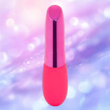 The Nu Sensuelle Nikita - Pink by NOVEL CREATIONS USA stands upright against a pastel purple and blue bokeh background, showcasing its sleek, rechargeable bullet vibrator design.