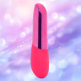 The Nu Sensuelle Nikita - Pink by NOVEL CREATIONS USA, a rechargeable silicone bullet vibrator, stands upright against a soft, blurred purple and pink background with circular light effects.