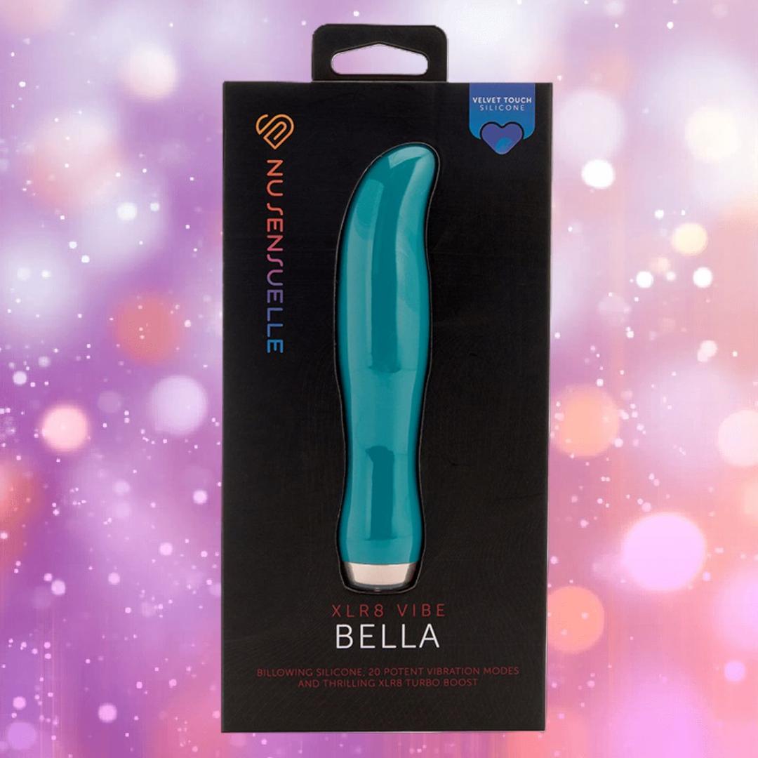 Presented against a blurred pink and purple bokeh background, the "Nu Sensuelle Velvet Touch Bella - Emerald Green" by NOVEL CREATIONS USA offers 20 vibration modes, XLR8 turbo boost, and velvet touch silicone for internal and external use.