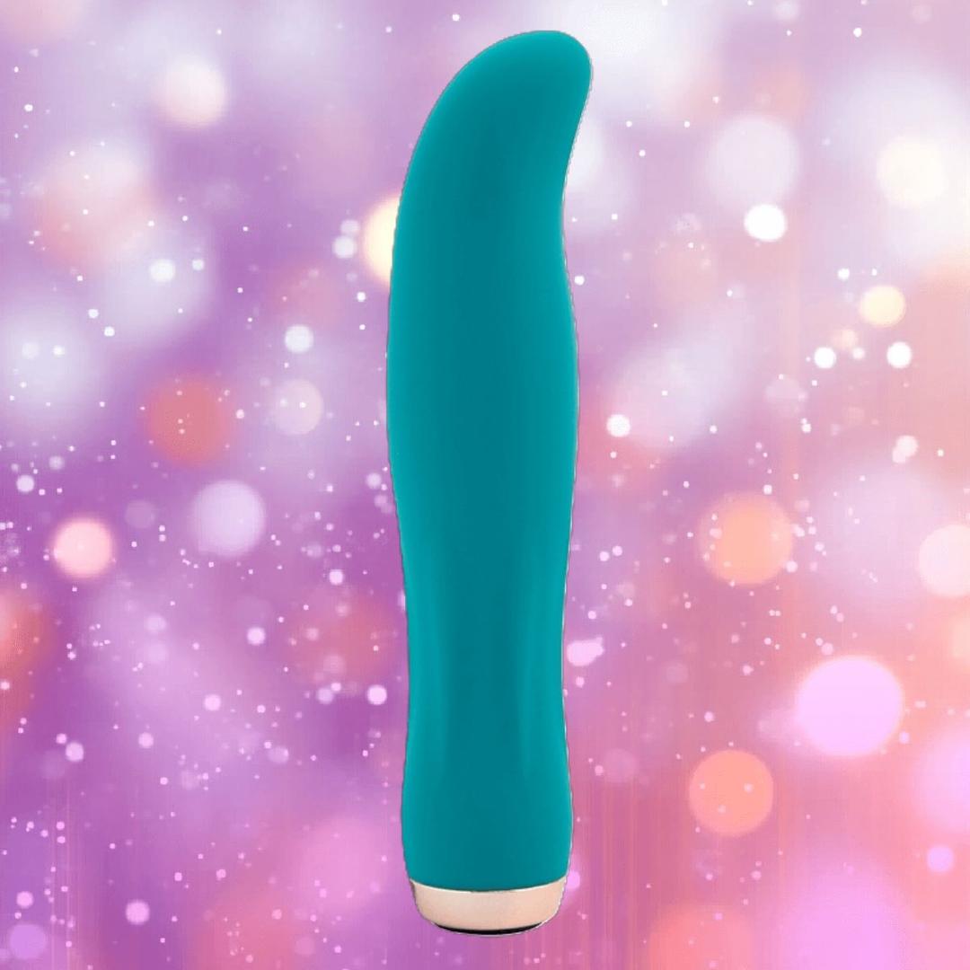 The Nu Sensuelle Velvet Touch Bella by NOVEL CREATIONS USA in emerald green stands upright against a blurred background with pink, purple, and orange bokeh lights, crafted from velvet touch liquid silicone for luxurious sensations.