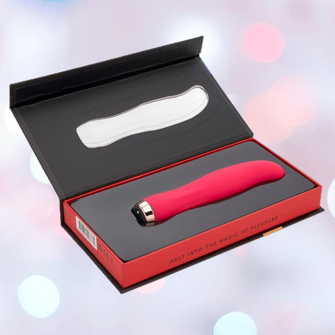 The Nu Sensuelle Velvet Touch Bella Vibrator with Turbo Boost in hot pink by NOVEL CREATIONS USA is displayed in a black and red box with the lid open, set against a soft pastel background. The molded interior fits the product perfectly.