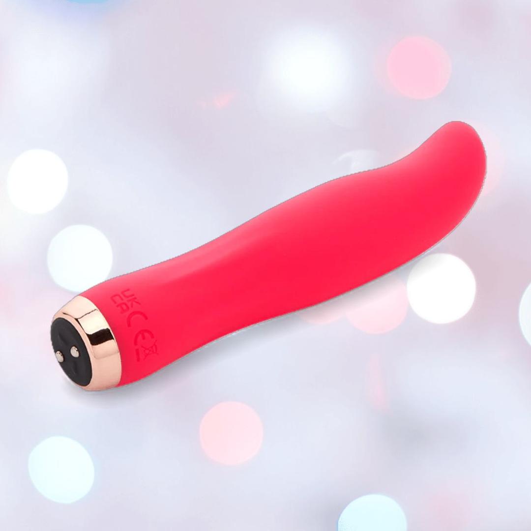 The Nu Sensuelle Velvet Touch Bella Vibrator with Turbo Boost in hot pink by NOVEL CREATIONS USA features a curved tip and gold-black base, displayed against a soft, blurred background with circular light spots.