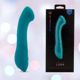 An emerald green, curved velvet touch silicone vibrator from NOVEL CREATIONS USA is shown beside its black "Nu Sensuelle Velvet Touch Luna Vibrator with Turbo Boost" box against a dreamy pastel bokeh background.