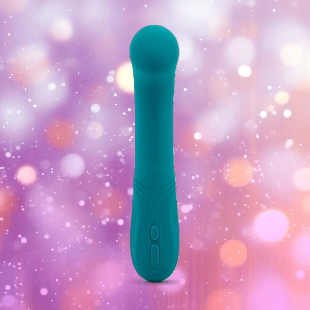 The Nu Sensuelle Velvet Touch Luna by NOVEL CREATIONS USA, an emerald green personal massager with control buttons, stands upright against a blurred pink and purple bokeh background.