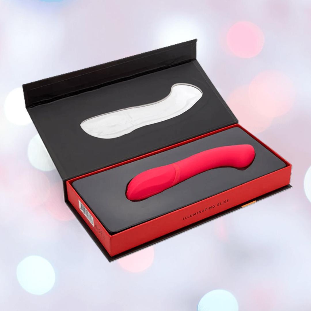 The Nu Sensuelle Velvet Touch Luna Vibrator with Turbo Boost by NOVEL CREATIONS USA is a hot pink, curved silicone toy offering 20 vibration patterns. Waterproof, it comes in a black and red box with molded insert, shown against a soft pink and blue background.