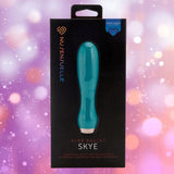 An emerald green Nu Sensuelle Velvet Touch Skye bullet vibrator by NOVEL CREATIONS USA in sleek black packaging with a purple and pink bokeh background. The box highlights "velvet touch silicone," "20 powerful vibrations," and the XLR8 turbo boost.