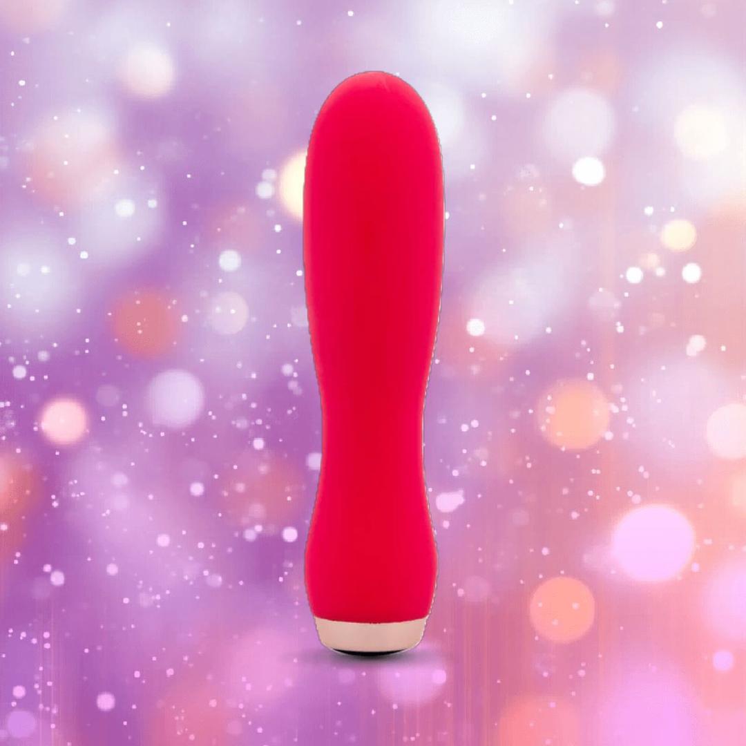 The Nu Sensuelle Velvet Touch Skye by NOVEL CREATIONS USA is a hot pink, cylindrical bullet vibrator with velvet-touch silicone, shown standing upright before a backdrop of purple and peach bokeh lights.