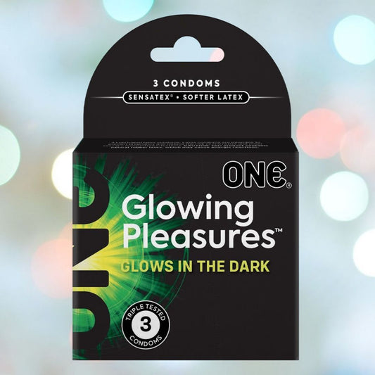 A sleek black box branded as "ONE Glowing Pleasure" presents glow-in-the-dark condoms crafted from natural rubber latex. The package emphasizes its "Senastex Softer Latex" and includes three triple-tested condoms, ideal for intimate occasions. The background is adorned with a bokeh effect comprised of gentle pastel lights. 1080