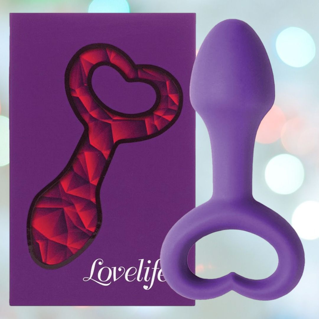 The OhMiBod Lovelife Explore Butt Plug in purple, featuring a heart-shaped handle, is displayed beside its branded box against a pastel background—an inviting choice from OhMiBod for shared adventures.