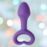 The OhMiBod Lovelife Explore Butt Plug in purple silicone, by OhMiBod, features a heart-shaped handle and is shown against a soft, pastel background—ideal for shared adventures.