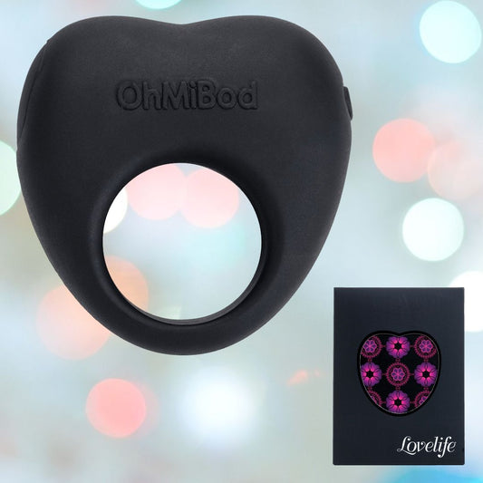 A black wearable ring-shaped product called the "OhMiBod Lovelife Share Couple’s Ring Vibe" is displayed against a blurred colorful background, evoking shared adventures. Next to it is a black box featuring a floral design and the word "Lovelife," symbolizing meaningful connections with its sensual aesthetic. 1080