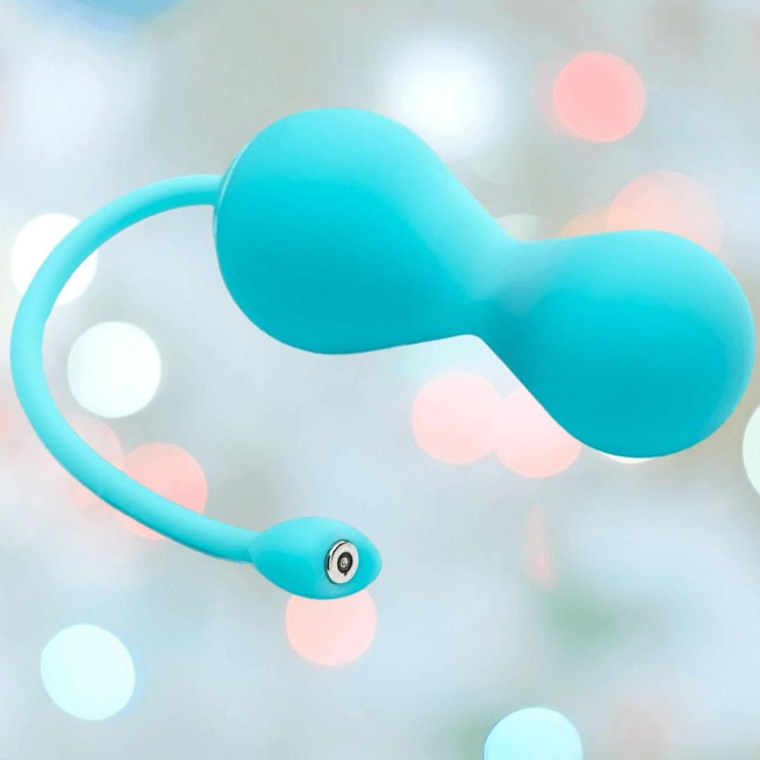 The OhMiBod Lovelife Krush Smart Kegel Fitness in turquoise is a Bluetooth app-connected silicone pelvic floor trainer with a bulbous double-ended shape and flexible tail, shown against a blurred background with pastel bokeh lights.