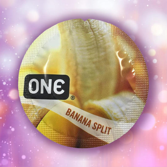 A round ONE Banana Split Flavored Condoms 🍌 wrapper shows a peeled banana and "ONE" branding, set against a blurred pink and purple bokeh background. 1080