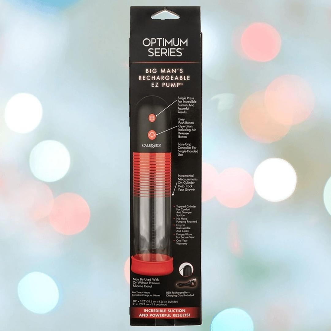 An upright, packaged CalExotics Optimum Series Big Man’s Rechargeable EZ Pump is shown in a black box with red accents, product details, branding, and device images against a blurred colorful background.