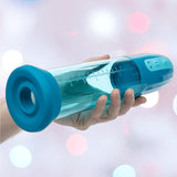 A hand holds the CalExotics Optimum Series Rechargeable Advanced Waterproof Pump, a transparent cylindrical device with blue ends and a measurement scale, set against a softly blurred pink, blue, and white bokeh background.