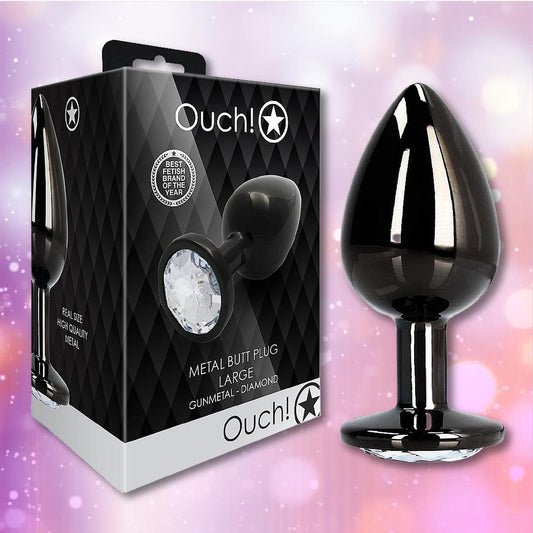 A Ouch! Large Metal Butt Plug – Gunmetal with Diamond Base by Shots stands beside its black, diamond-patterned box. The shimmering pastel background highlights the plug’s sparkling gem base. 1080