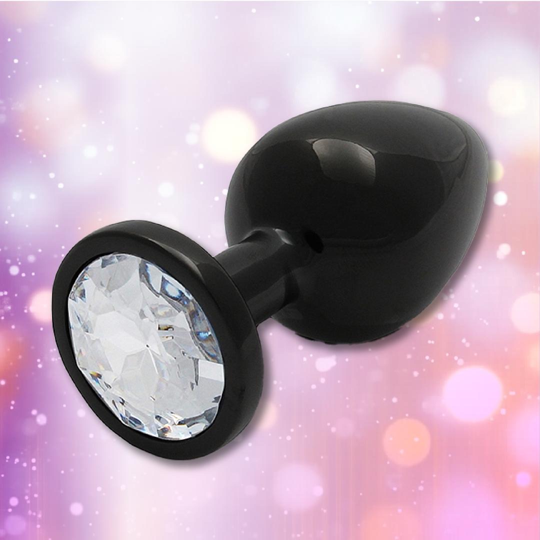 The Ouch! Large Metal Butt Plug – Gunmetal with Diamond Base by Shots gleams against a soft, colorful bokeh background filled with pink, purple, and white light spots.