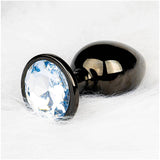 The Ouch! Large Metal Butt Plug by Shots features a smooth gunmetal finish and a large, clear diamond base, displayed on a soft white surface.