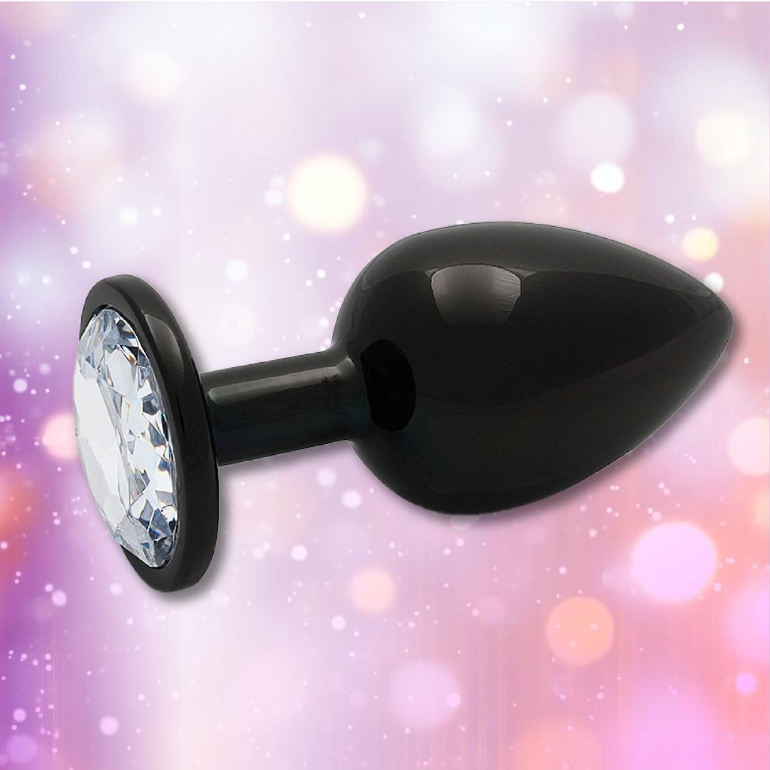 The Ouch! Large Metal Butt Plug – Gunmetal with Diamond Base by Shots is shown against a blurred, colorful background with pink and purple bokeh lights.
