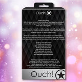 The image displays the back packaging of the Shots Ouch! Large Metal Butt Plug – Gunmetal with Diamond Base, featuring a product description, key features, and company contact info on a black diamond-patterned background with blurred pastel accents.