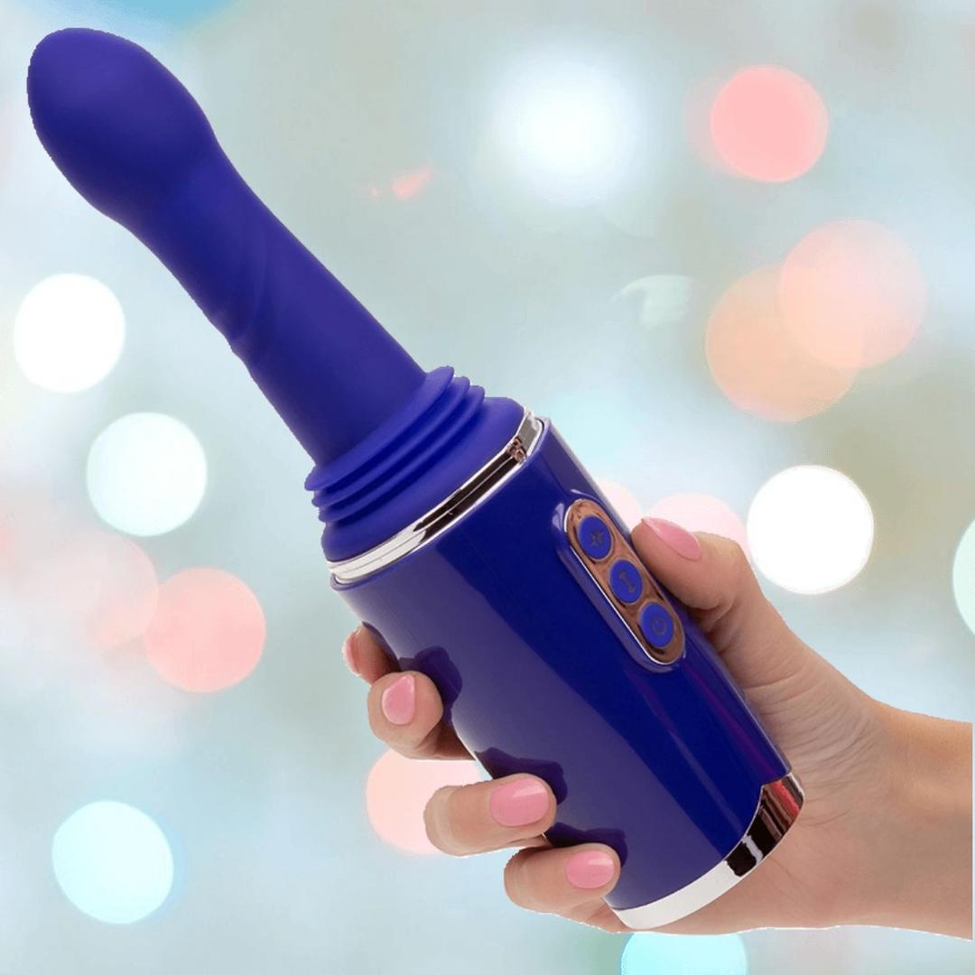 A hand with pink-painted nails holds the CalExotics Overdrive Portable Sex Machine Travel Thruster, a blue, wand-shaped device with buttons and a flexible, ribbed attachment, against a blurred, colorful background.