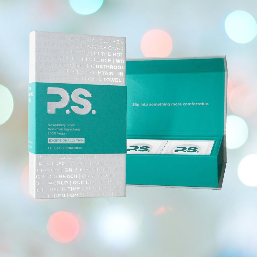 A box of P.S. Ultra-Thin Vegan Condoms is displayed. The teal and white packaging, featuring the slogan "Slip into something more comfortable," reveals its ultra-thin, vegan contents against a blurred bokeh backdrop.