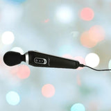 A BMS PalmPower Extreme Wand Massager in black with a rounded head is plugged in and suspended against a background featuring blurred colorful lights.
