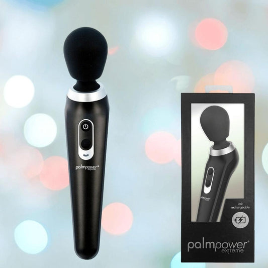 The BMS PalmPower Extreme Wand Massager – Black is shown with its packaging, featuring an image of the rechargeable device on the box. The scene is set against a background of softly blurred pastel lights. 1080