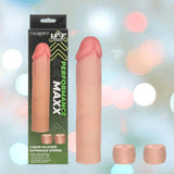 The CalExotics Performance Maxx Liquid Silicone Extension System - Ivory, shown with two extra silicone ring caps, is displayed beside its green and black box amid softly blurred colorful lights.