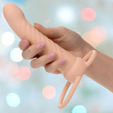 A hand with manicured nails holds the CalExotics Performance Maxx Rechargeable Ribbed Dual Penetrator in Ivory, featuring a textured shaft and dual looped handles, shown against a softly blurred pastel background.