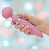 A hand holds the BMS Pillow Talk Sultry Wand Massager in pink, featuring a quilted handle and rounded head for G-spot stimulation, set against a softly blurred pastel background.