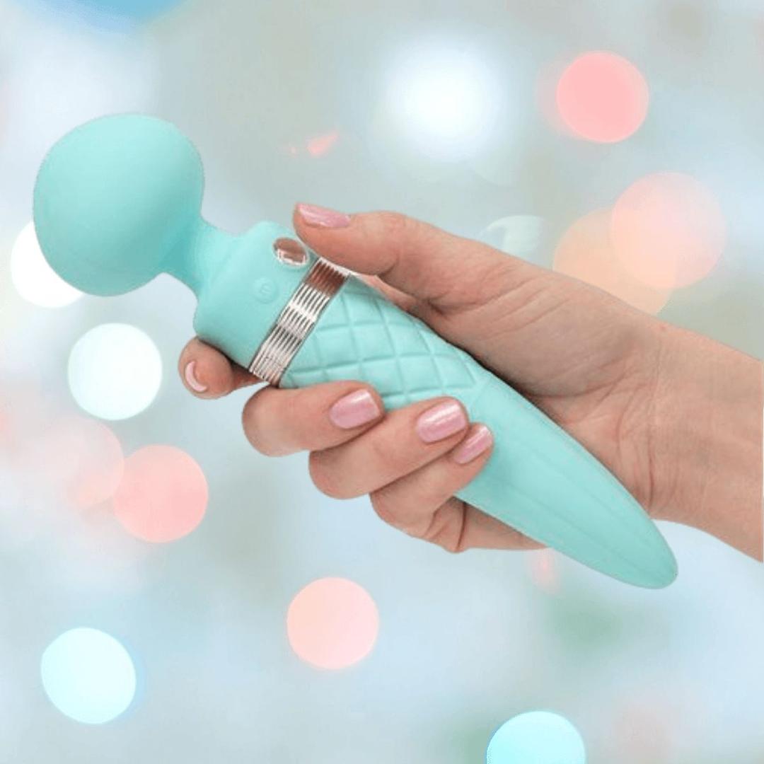 A manicured hand holds the Pillow Talk Sultry Wand Massager by BMS in teal—a turquoise, ice cream cone-shaped vibrator with a rounded head and textured handle—set against a blurred pastel background.