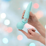 A person holds the BMS Pillow Talk Sultry Wand Massager in teal, featuring a quilted handle and rounded head for powerful vibrations, against a softly blurred pastel background.