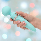 A manicured hand holds the Pillow Talk Sultry Wand Massager by BMS in teal—a turquoise, ice cream cone-shaped vibrator with a rounded head and textured handle—set against a blurred pastel background.