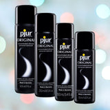 Four bottles of Pjur Original BodyGlide Silicone Lubricant from the Pjur brand are displayed against a blurred bokeh background. The hypoallergenic bottles range in size from 30ml to 500ml, and are all black with white and gray text. Each bottle is labeled "Made in Germany.