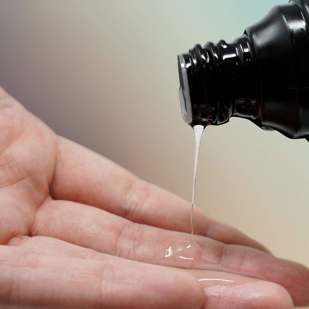 A hand being filled with Pjur AQUA Water-Based Lubricant, a clear liquid pouring from a dark-colored bottle, highlights the use of this 100ml (3.4oz) product. The soothing background is softly blurred, showcasing its application in skincare or cosmetics.